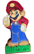 Piñata artesanal temática de Súper Mario Bros con acabados brillantes en colores rojo, azul y beige, decorada sobre una base de césped verde. Ideal para fiestas infantiles, cumpleaños y eventos temáticos de videojuegos. 